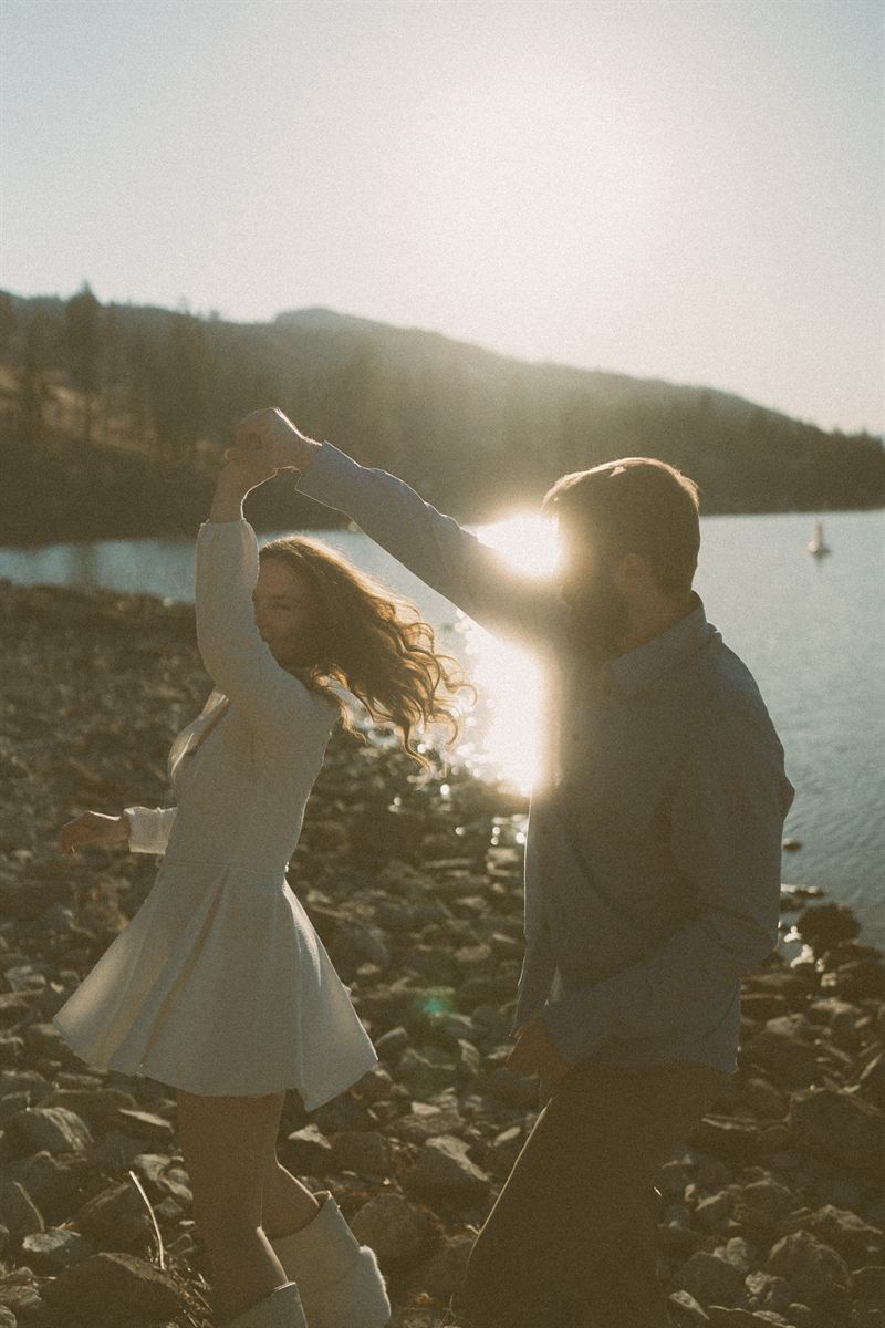 He spins her on the rocks at the edge of Okanagan Lake, a sailboat out on the water behind them