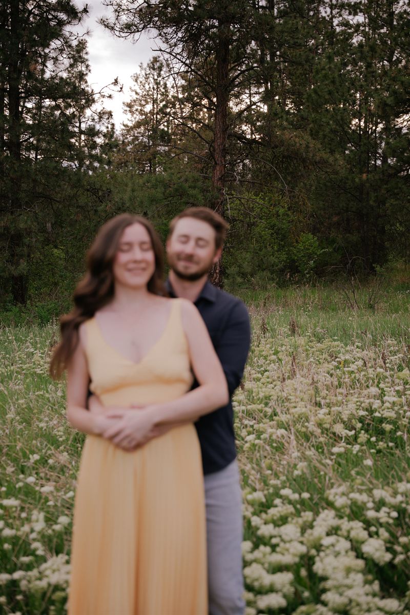 Soft-focus portrait of a couple holding each other in a meadow of wild yarrow, ponderosa pines behind them