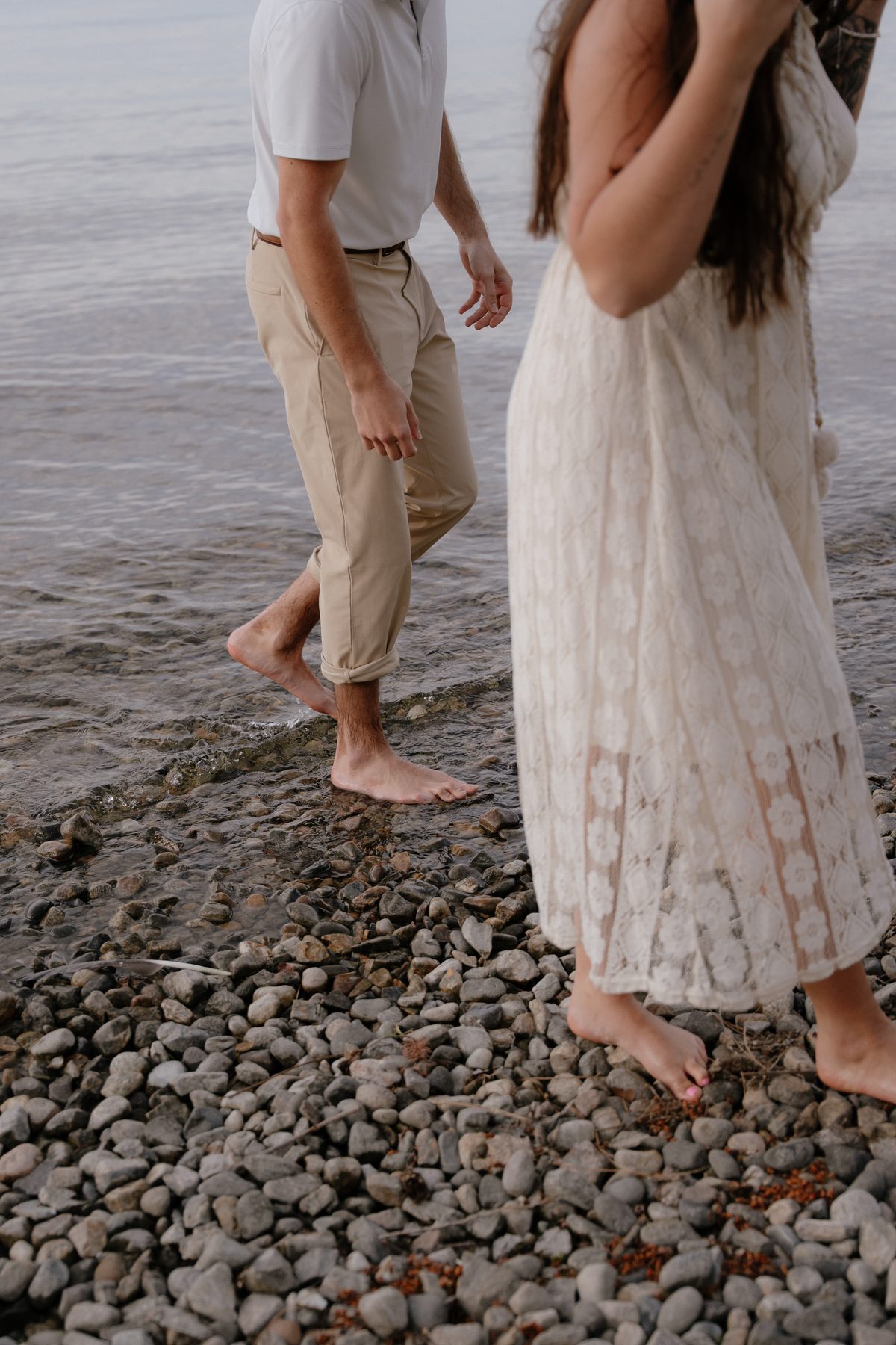 Barefoot on the smooth stones at the edge of Okanagan Lake, a couple walking into the shallows