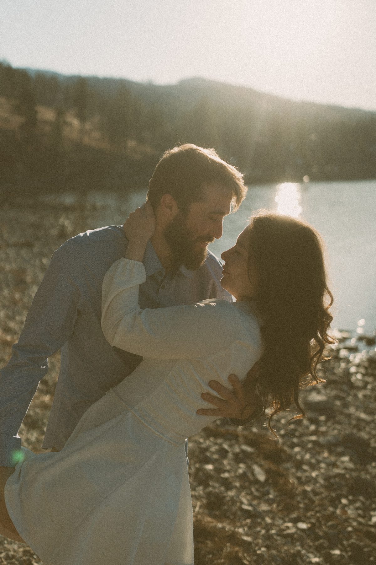He dips her for a kiss on the rocky shore of Okanagan Lake, sun flaring off the water