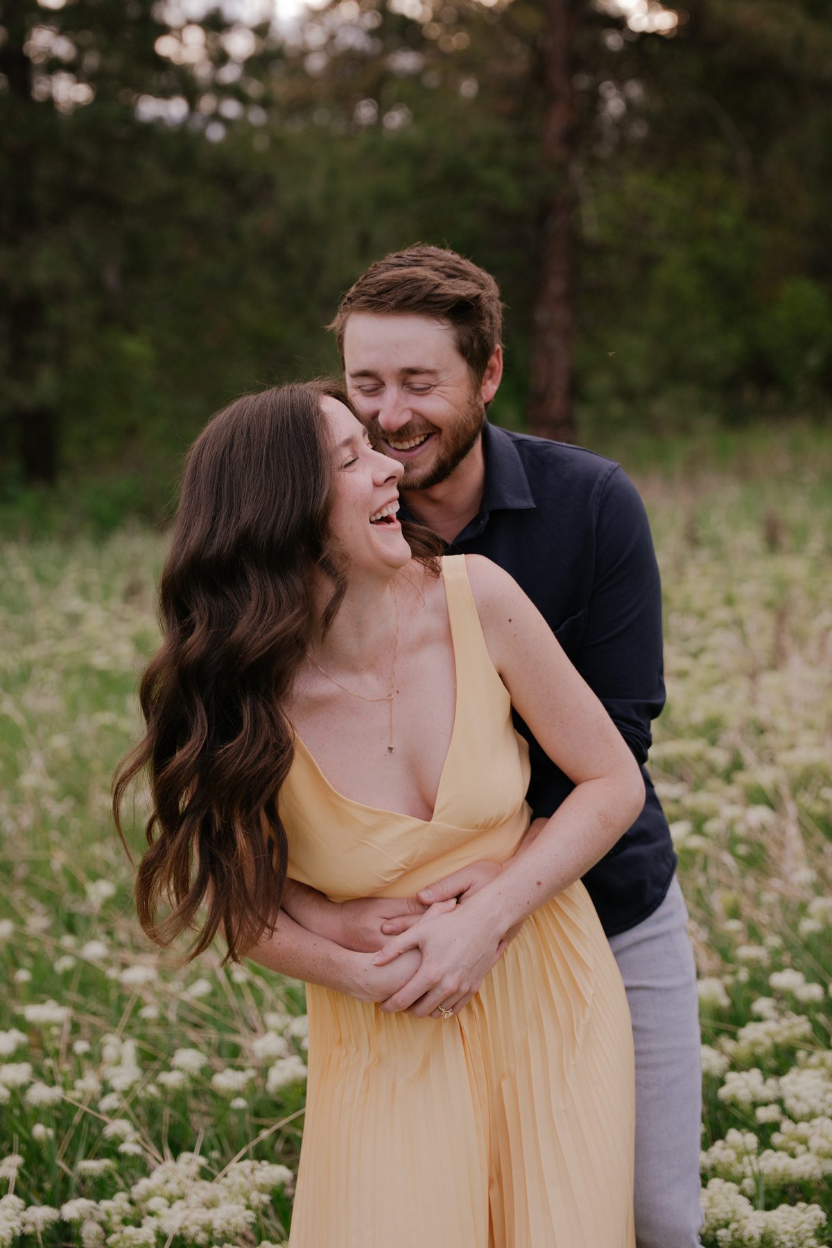 She laughs as he wraps his arms around her from behind in an Okanagan field of white wildflowers