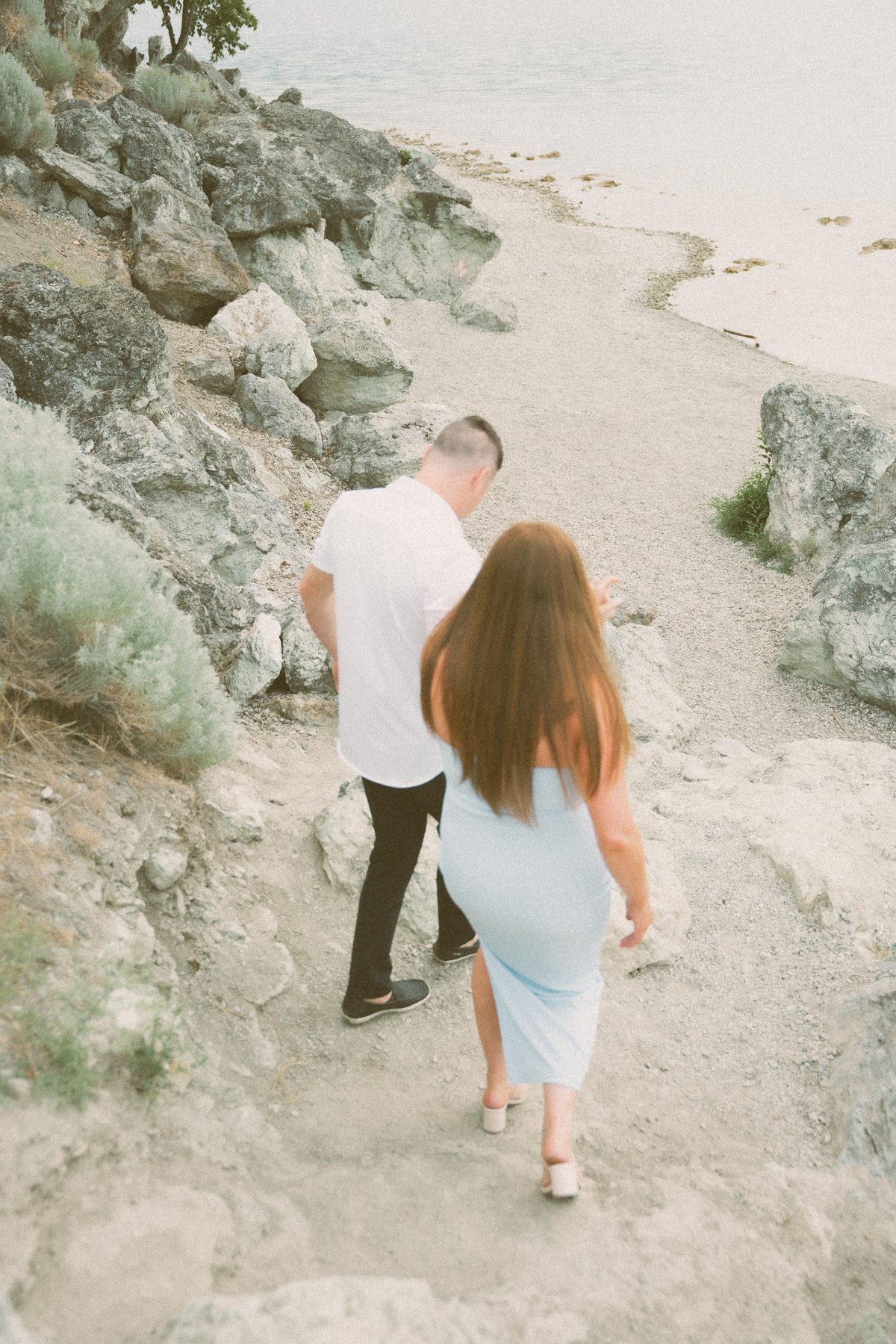 Looking down on a couple picking their way along a rocky path to the lakeshore below