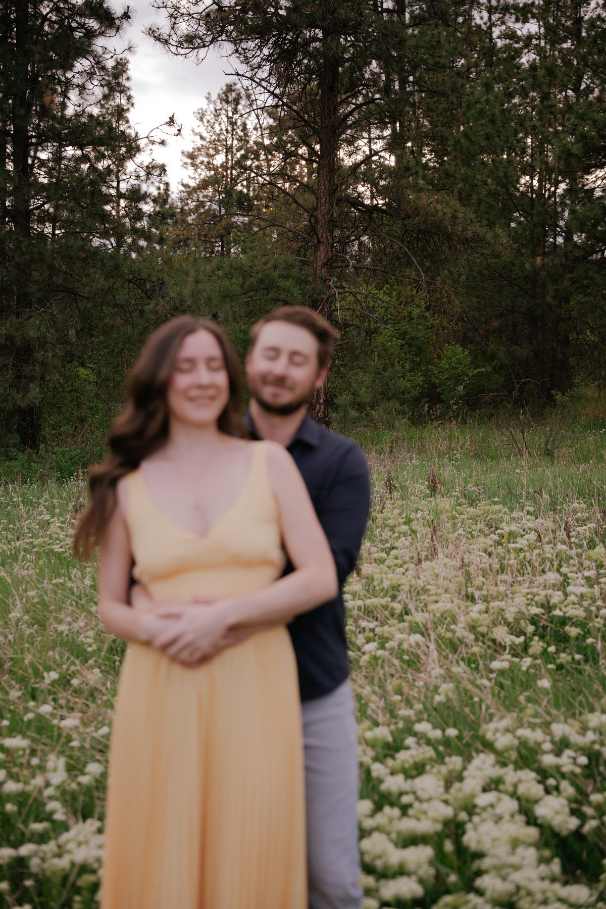 Soft-focus portrait of a couple holding each other in a meadow of wild yarrow, ponderosa pines behind them