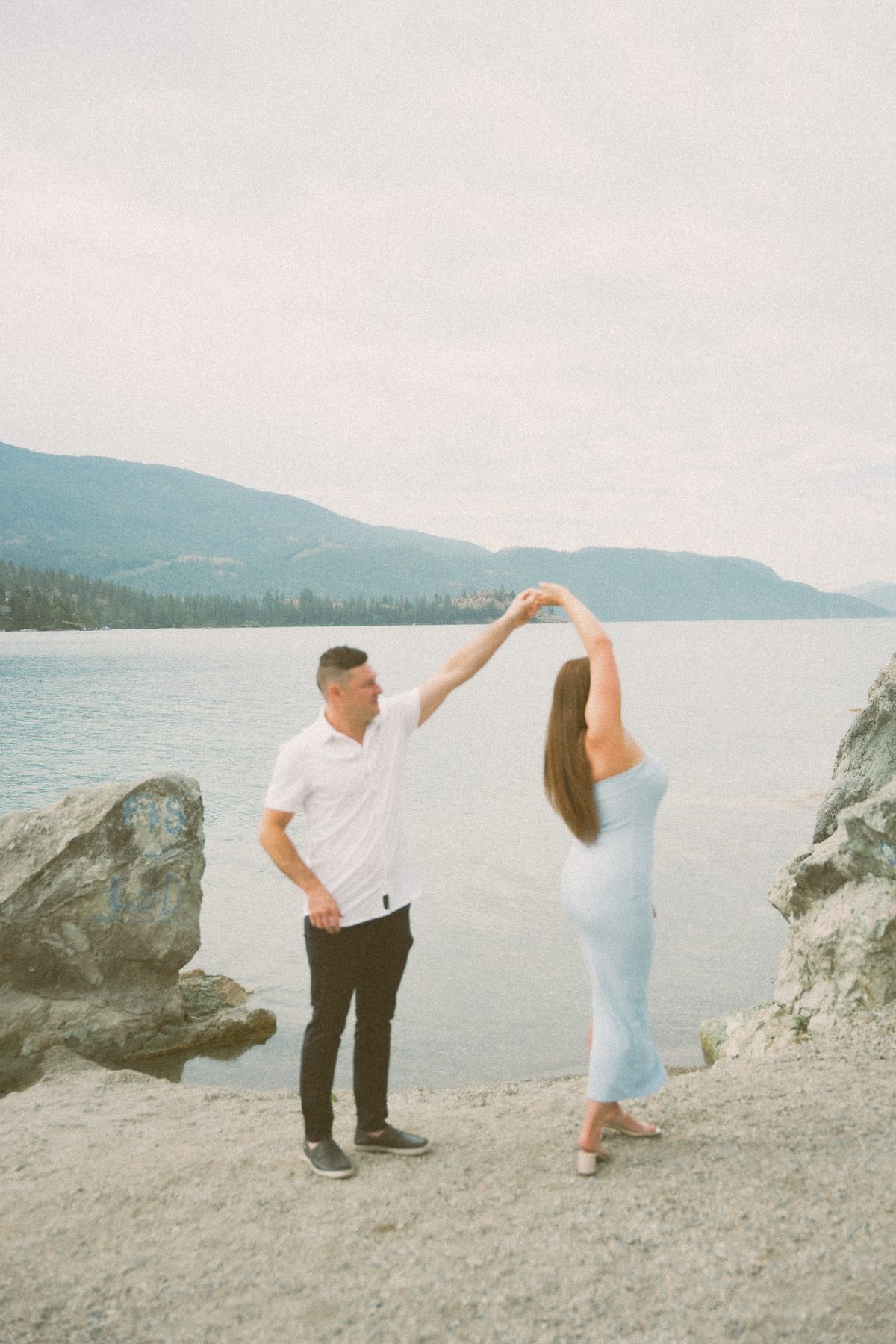 He spins her on a gravel beach beside Okanagan Lake, forested hills rising across the water