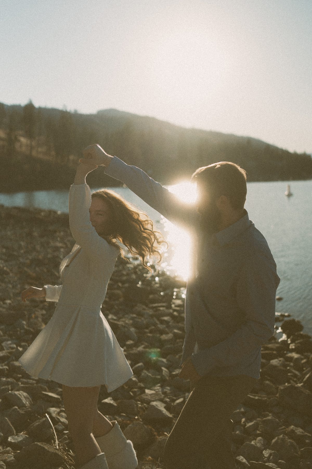 He spins her on the rocks at the edge of Okanagan Lake, a sailboat out on the water behind them