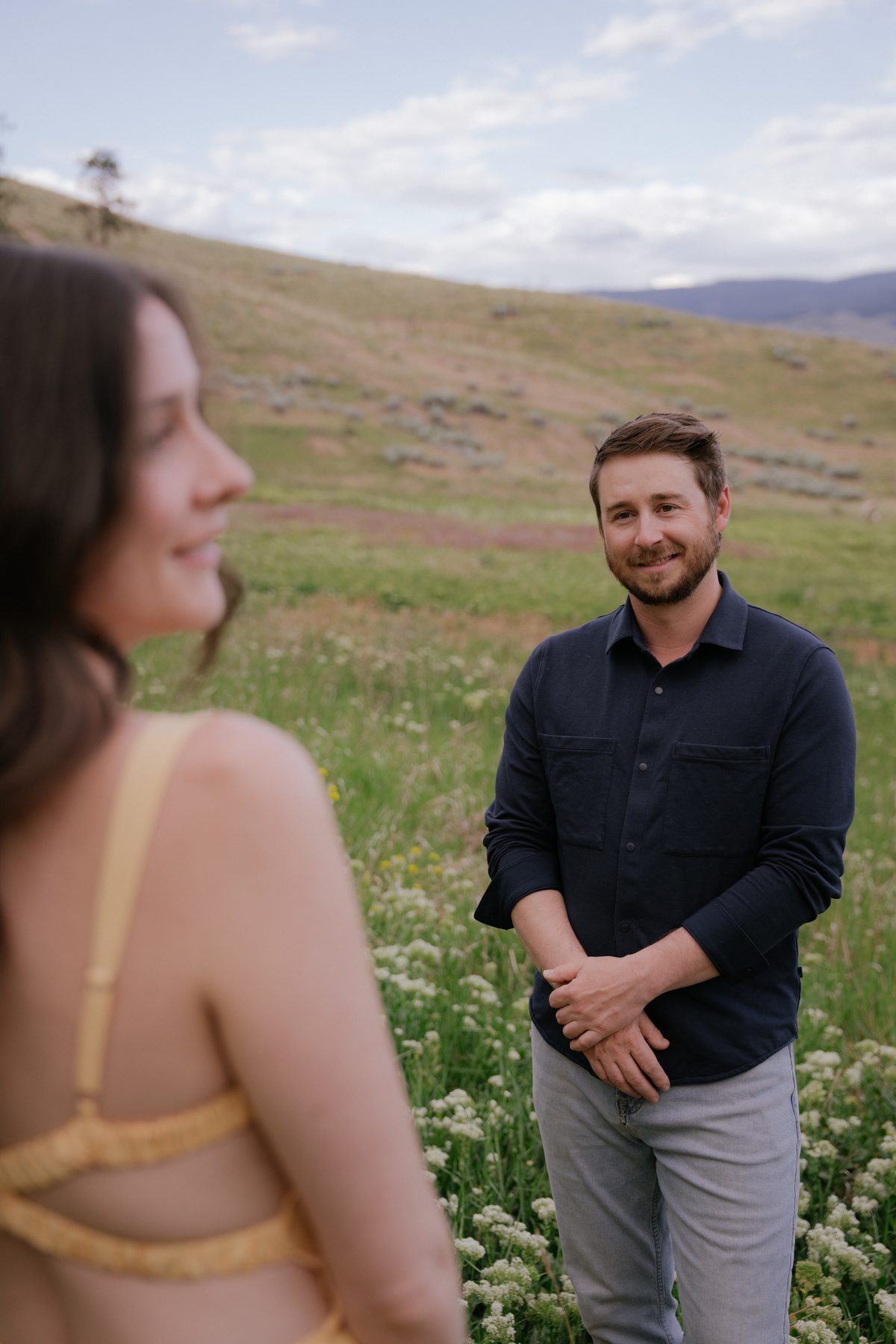 He watches her across a wildflower meadow, the grassy hills of the Okanagan rising behind him