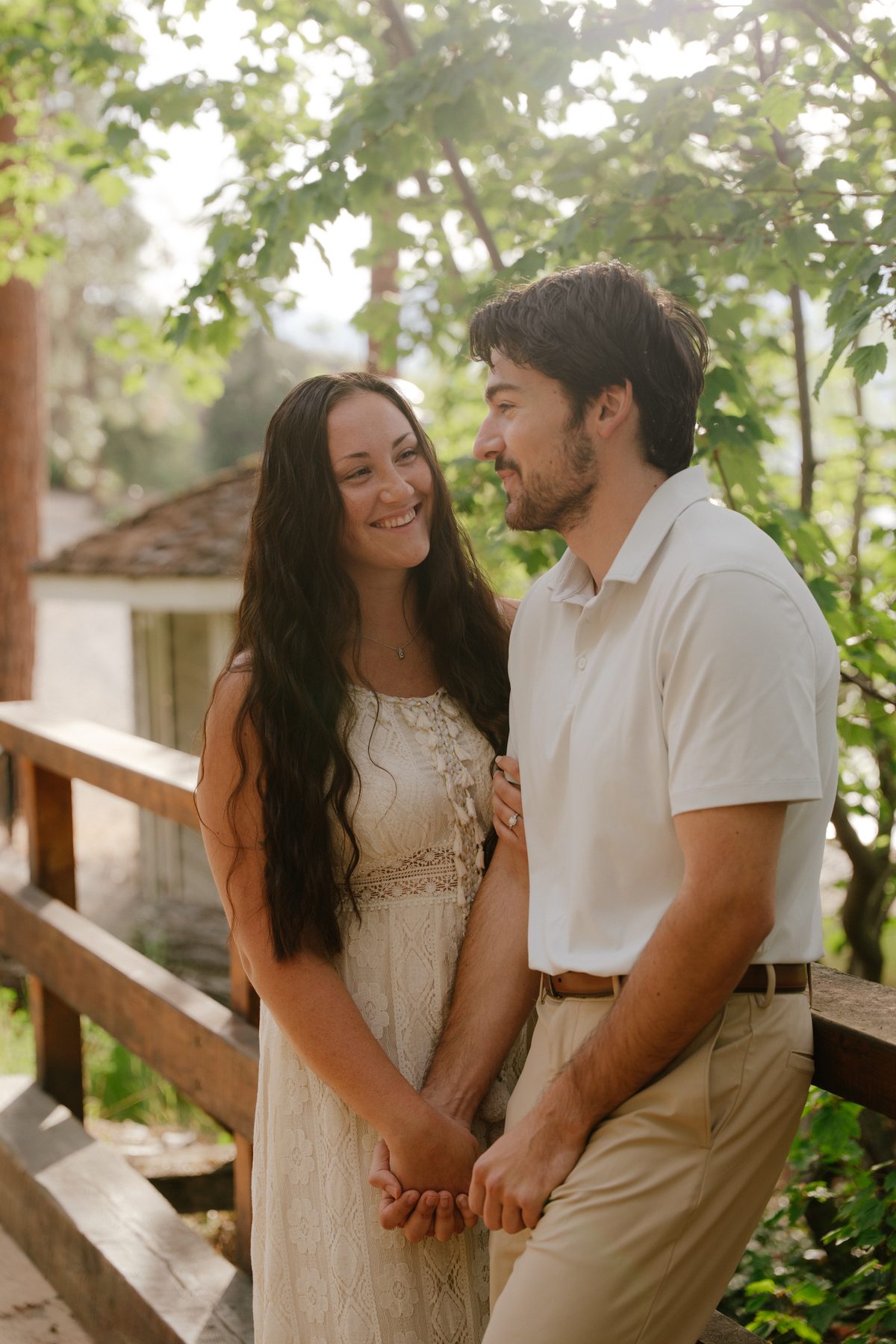 Engaged couple holding hands on a wooden bridge in dappled summer light