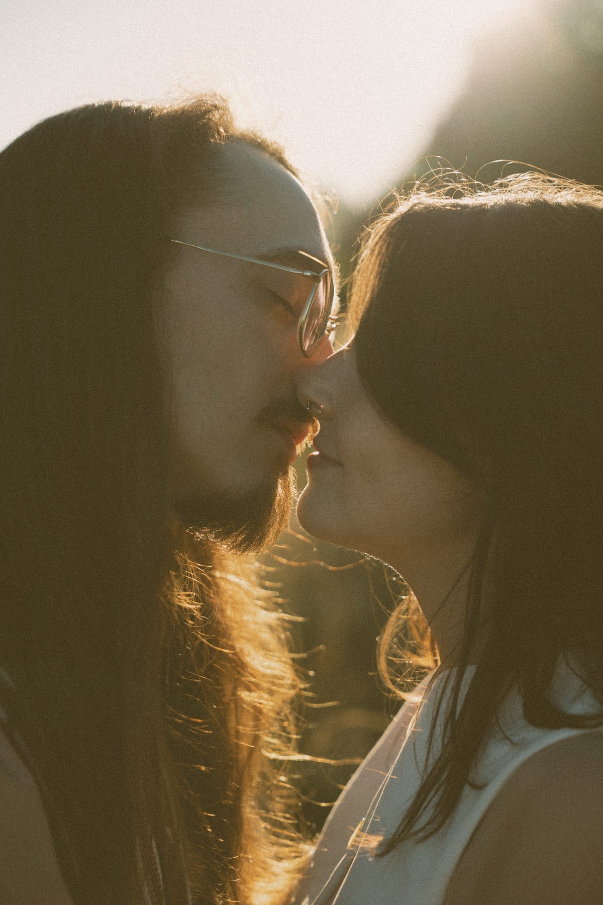 Backlit close-up of a couple about to kiss, sunlight catching in their hair