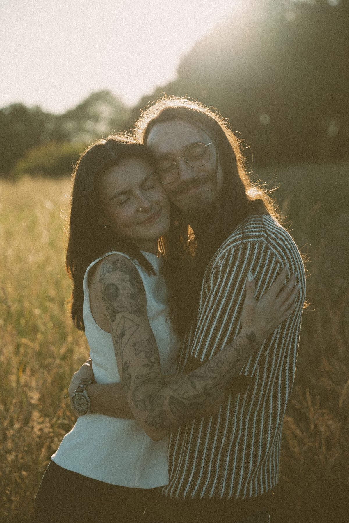 Couple holding each other in a sunlit Vancouver Island field, both of them with their eyes closed