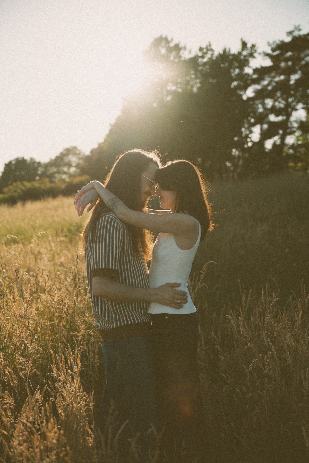 Couple holding each other in tall dry grass on Vancouver Island, sun flaring through the oaks