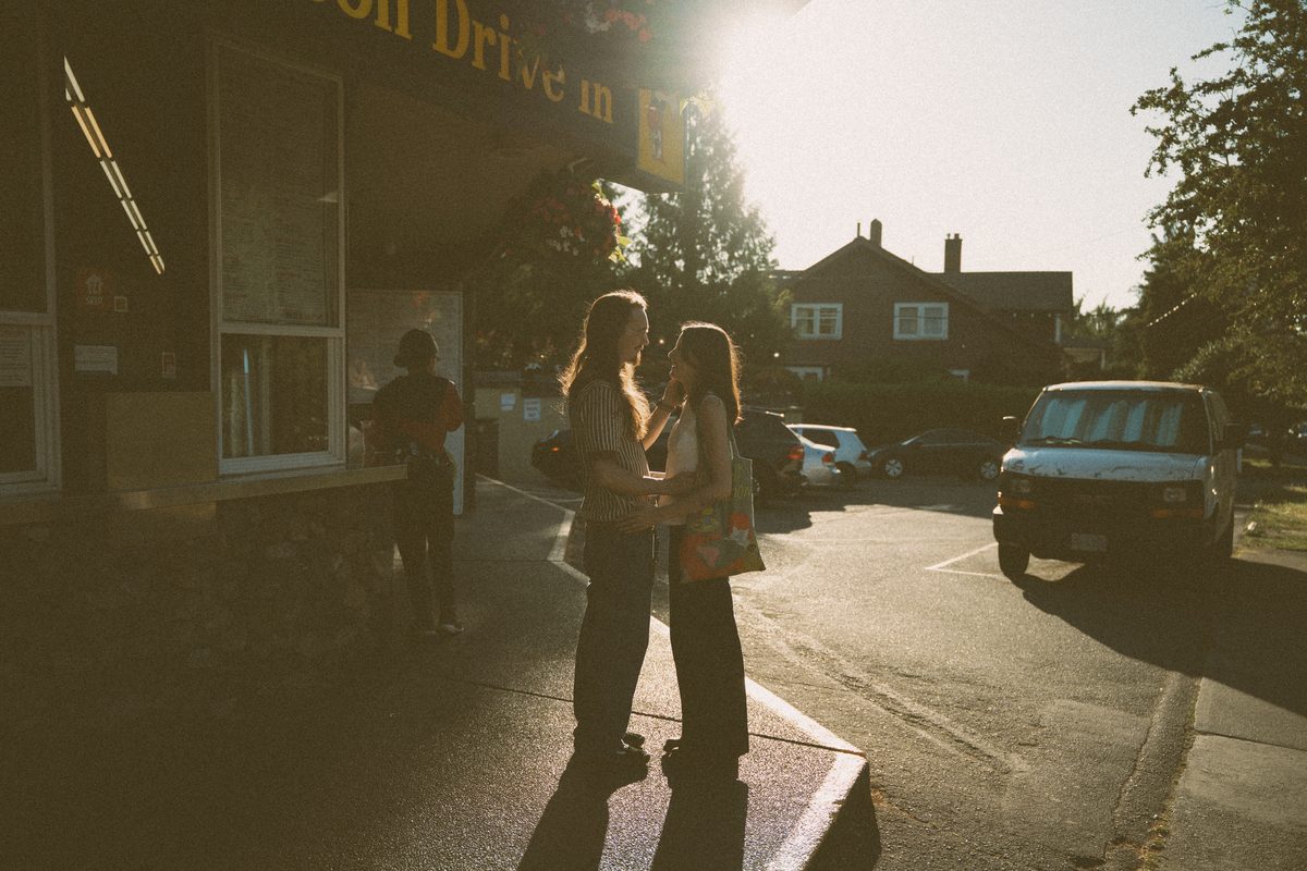 Engaged couple in the parking lot of a Victoria drive-in at golden hour, a tote bag over her shoulder