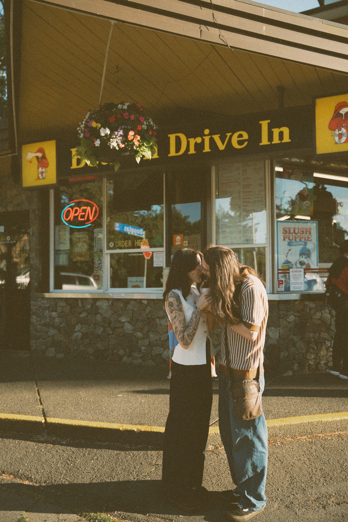 Couple kissing outside the Beacon Drive In in Victoria, BC, the neon open sign glowing in the window