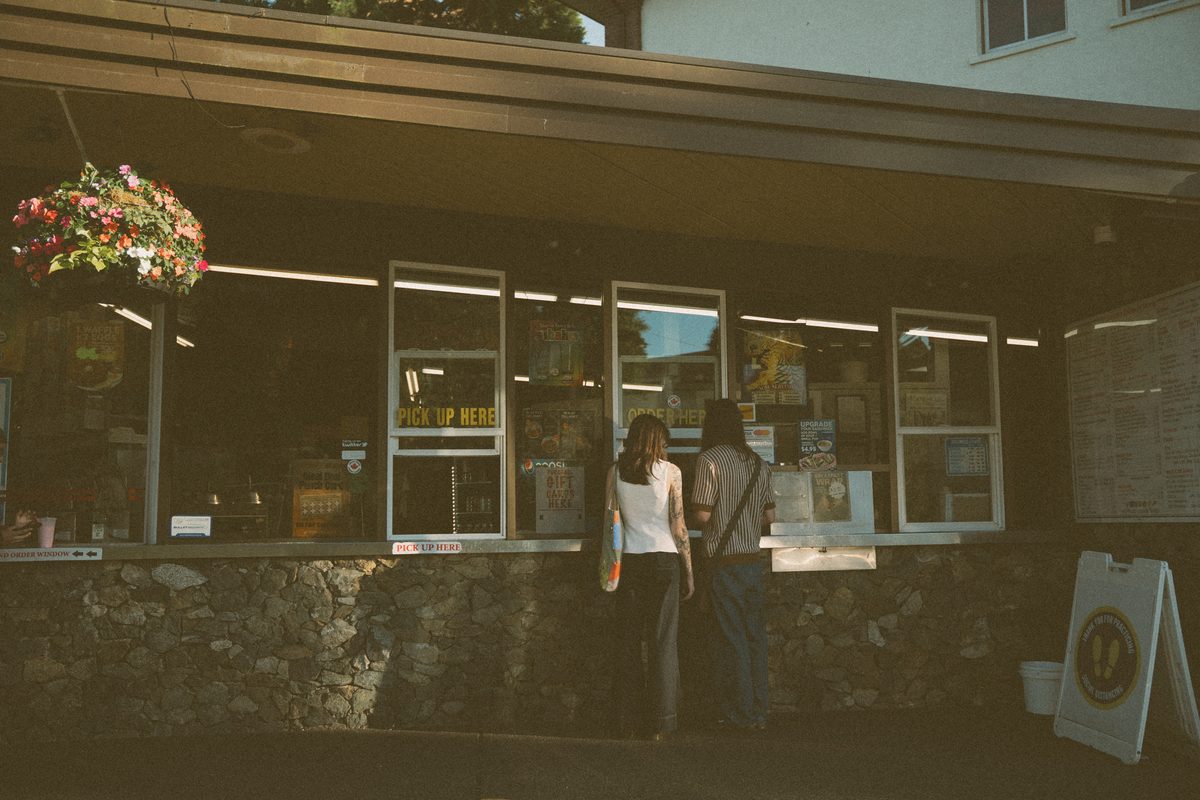 Couple ordering at the window of a Victoria drive-in, hanging flower baskets above them