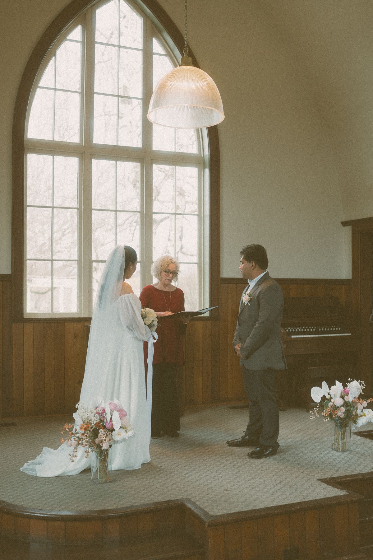 Carlith and Mark at the altar with their officiant in the window light