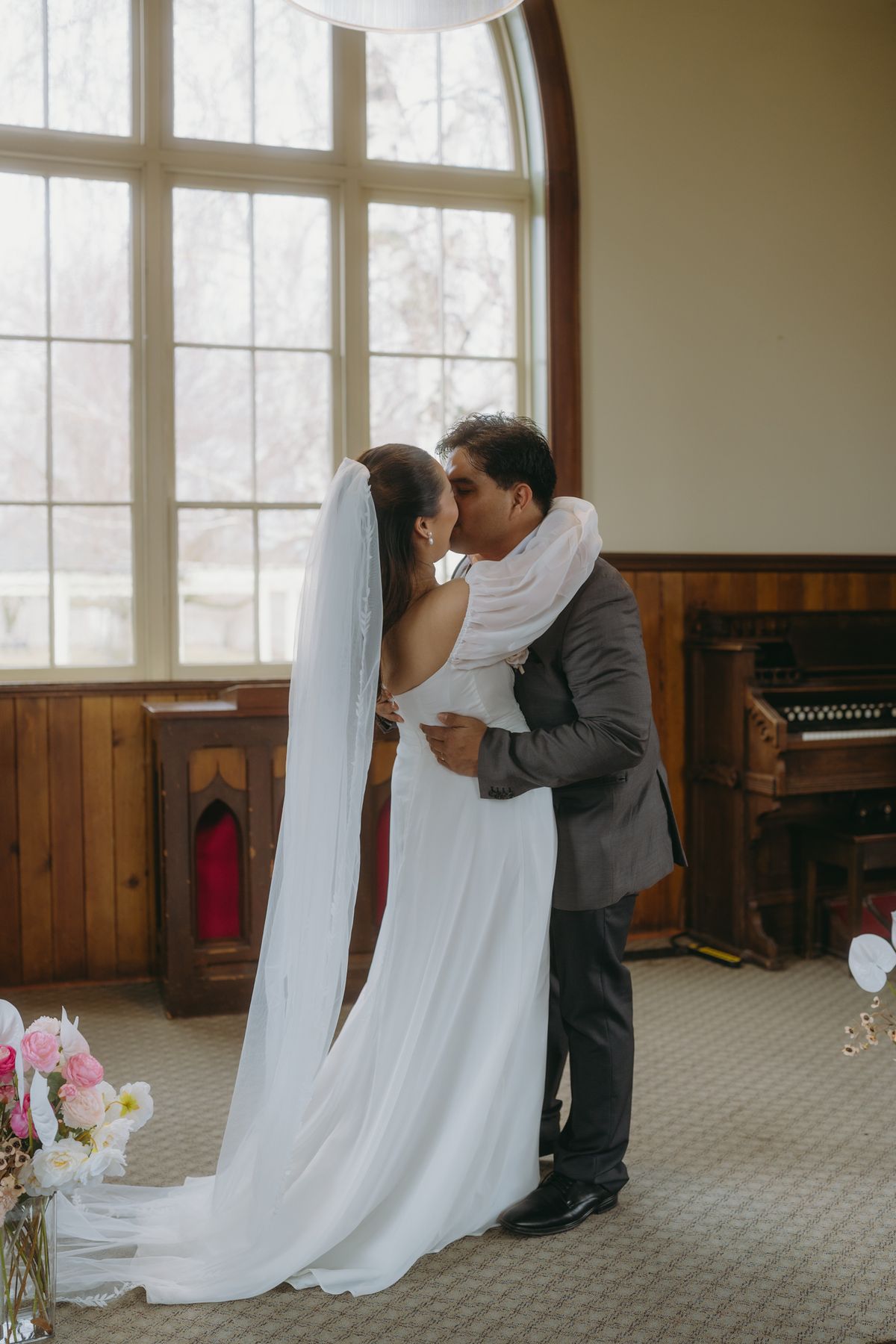 The couple sharing a kiss beside the arched window