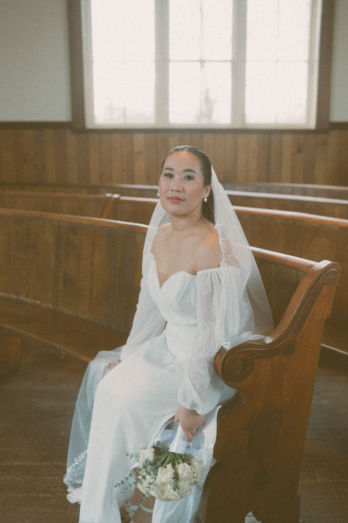 Bride seated in a pew with her veil and bouquet
