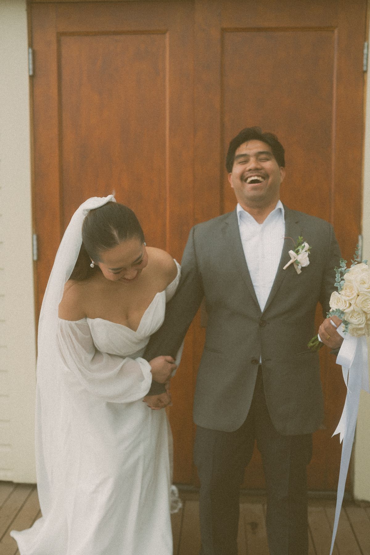 The couple laughing together against the church's wooden doors