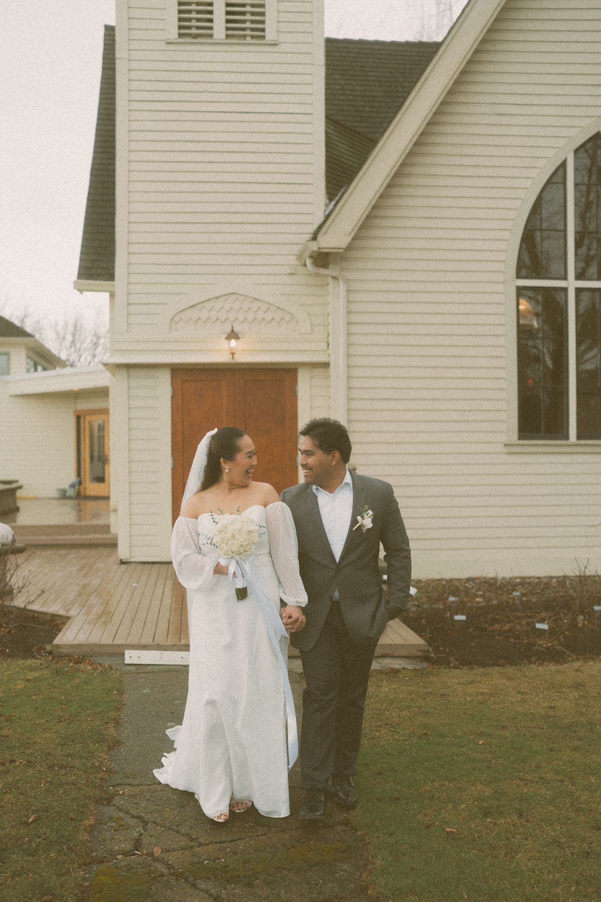 The newlyweds walking on the lawn outside the white heritage church