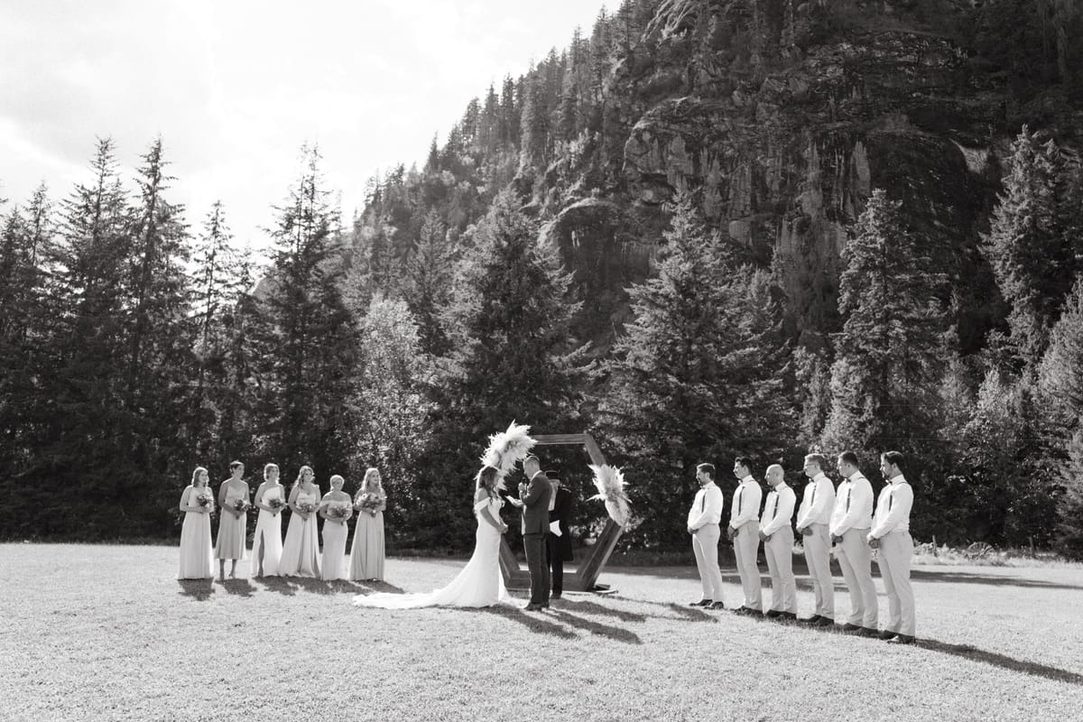 Black and white of the ceremony with the wedding party lined up below the rock face