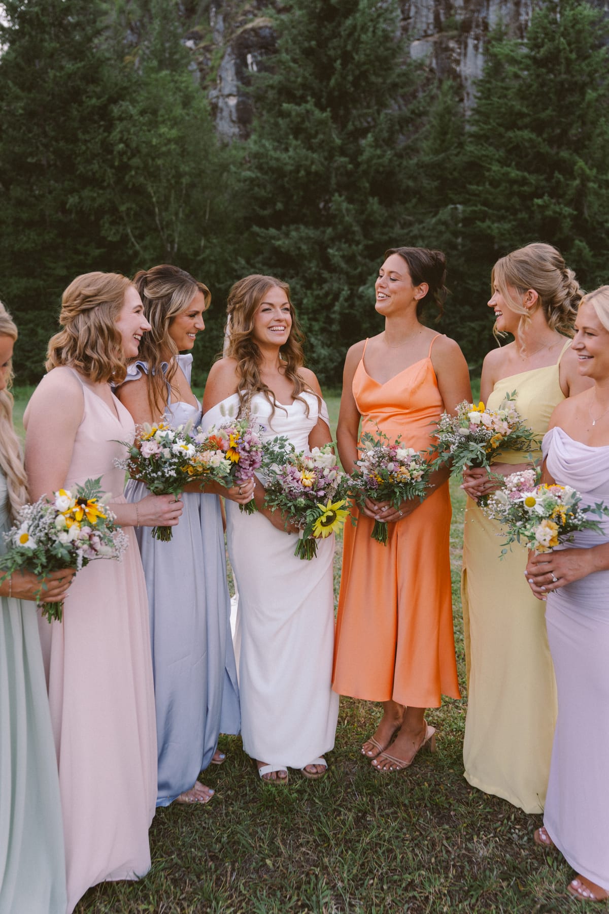 Kendra and her bridesmaids laughing with their wildflower bouquets, mountain behind