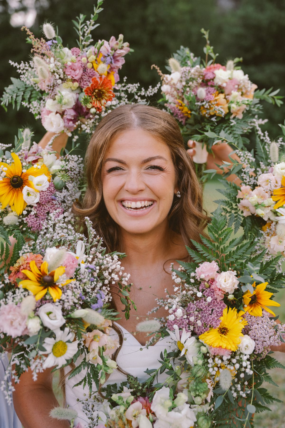 Kendra's smiling face framed by her bridesmaids' wildflower and sunflower bouquets