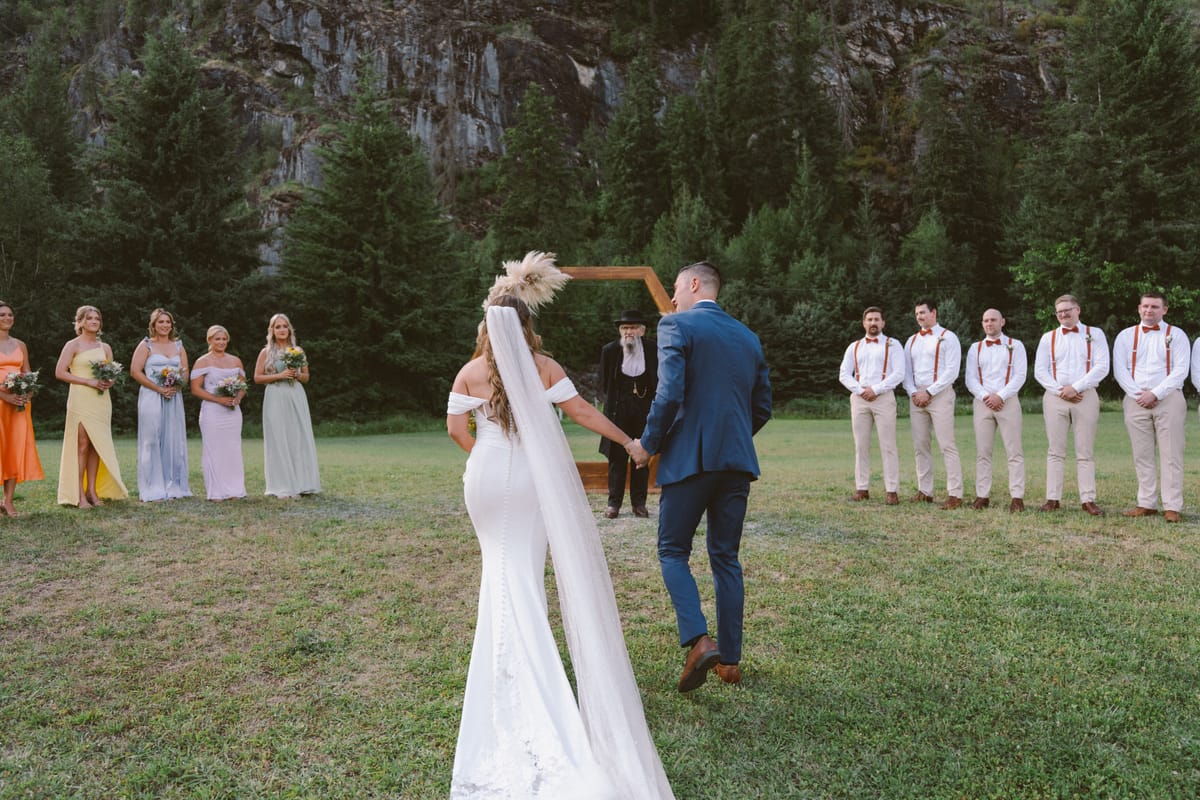Kendra and Rory holding hands at the hexagonal arch as the wedding party looks on