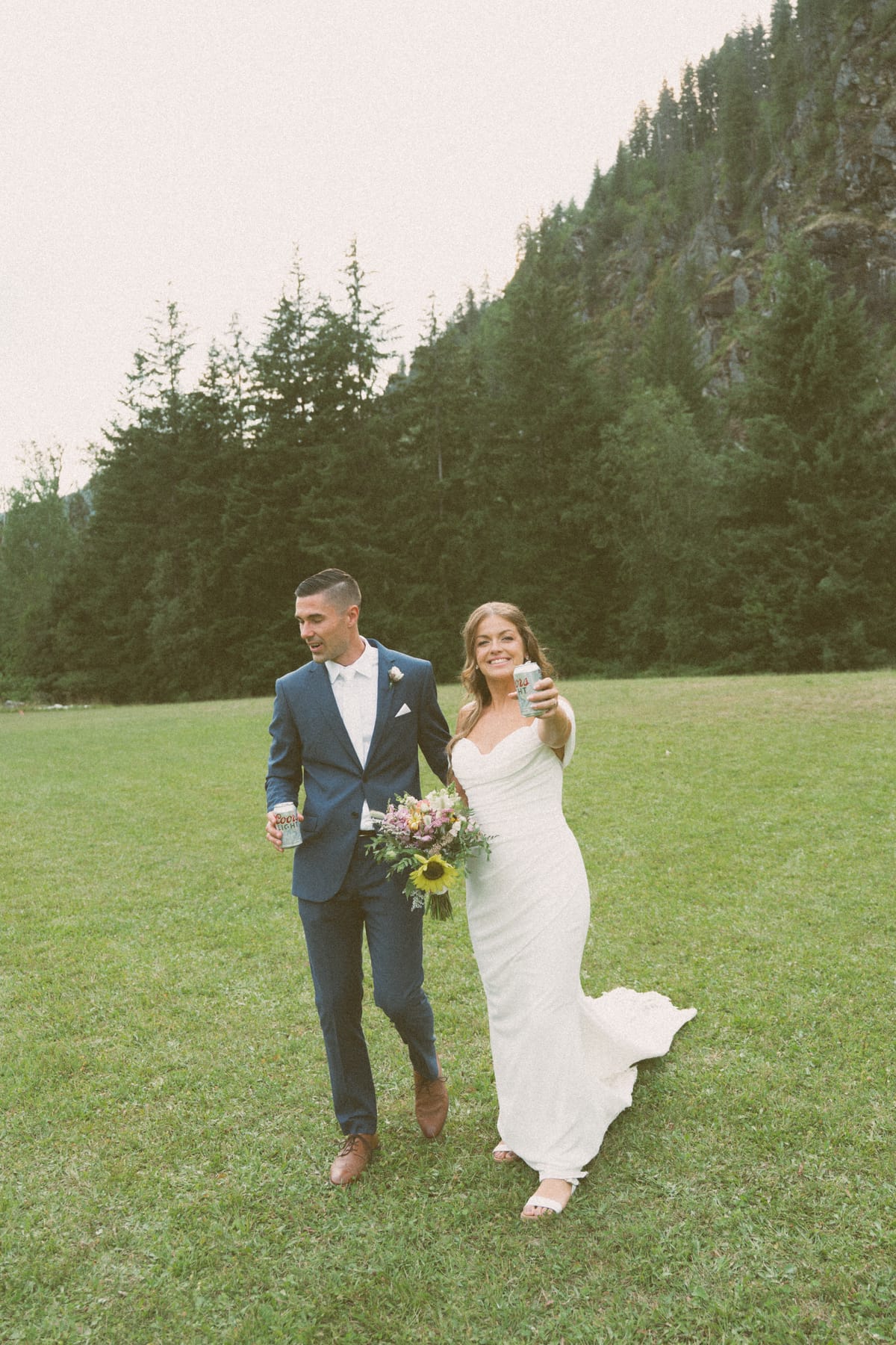 Kendra and Rory walking through the meadow with drinks in hand, mountain behind