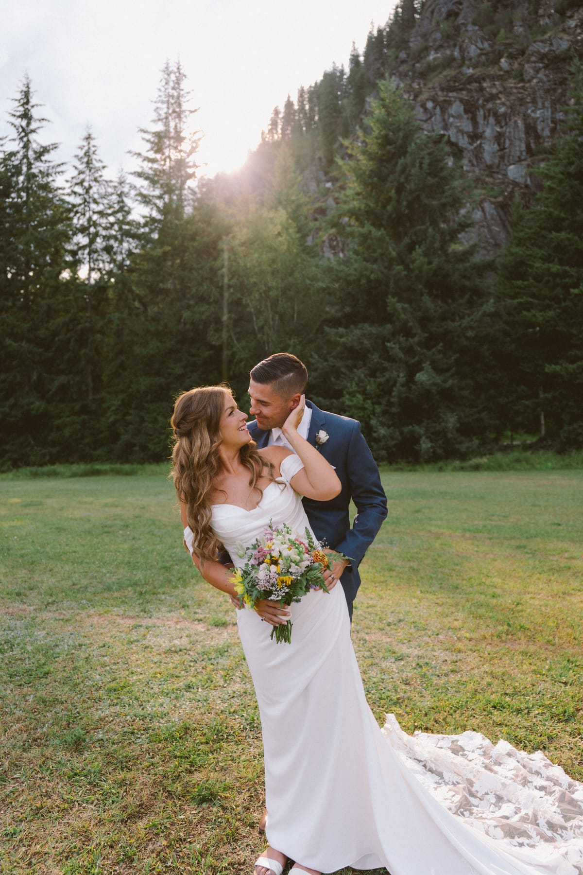 Kendra and Rory at golden hour in the meadow below the rock face, sun flaring over the trees
