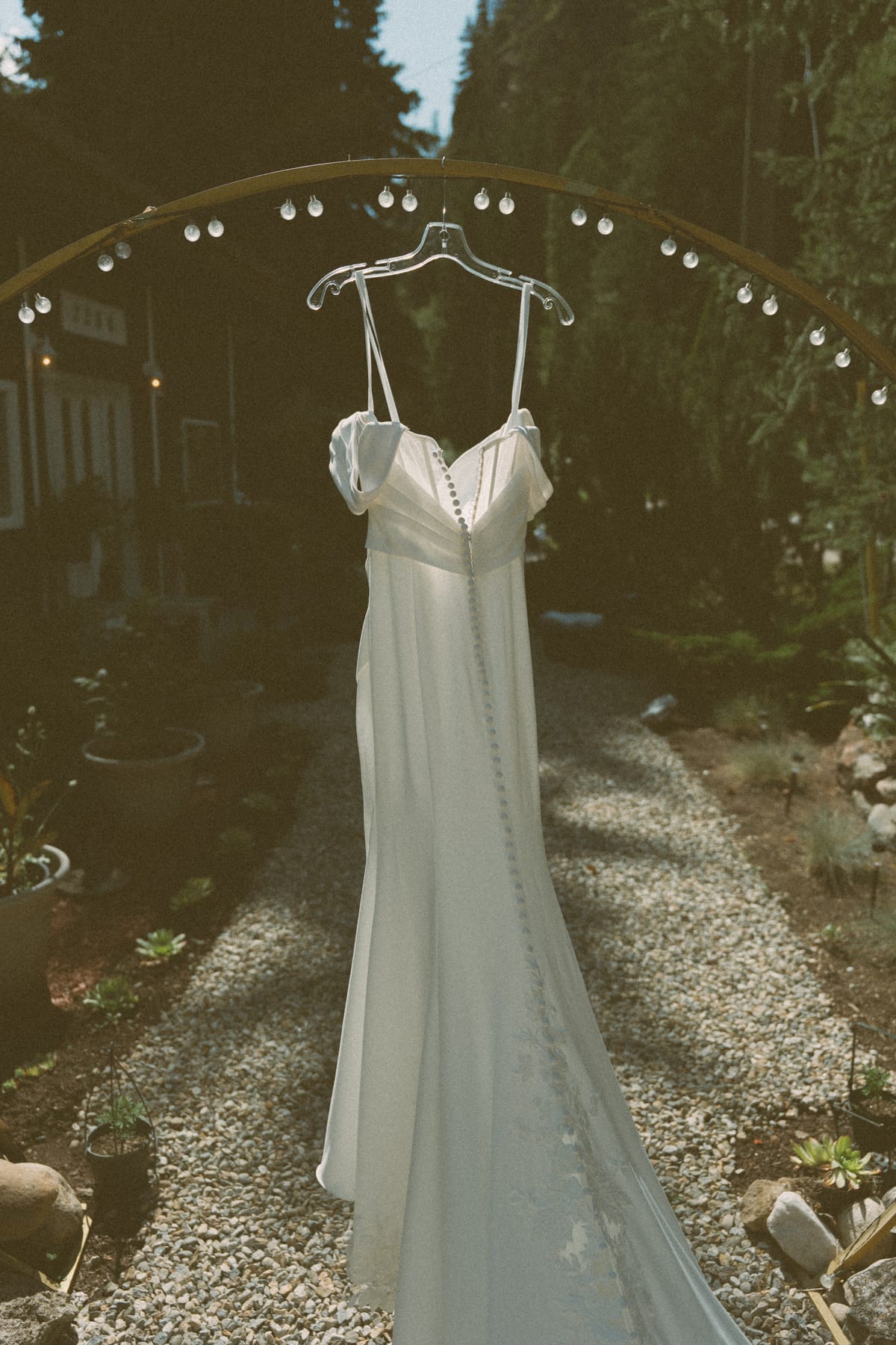 Kendra's satin gown hanging under a string-lit garden arch
