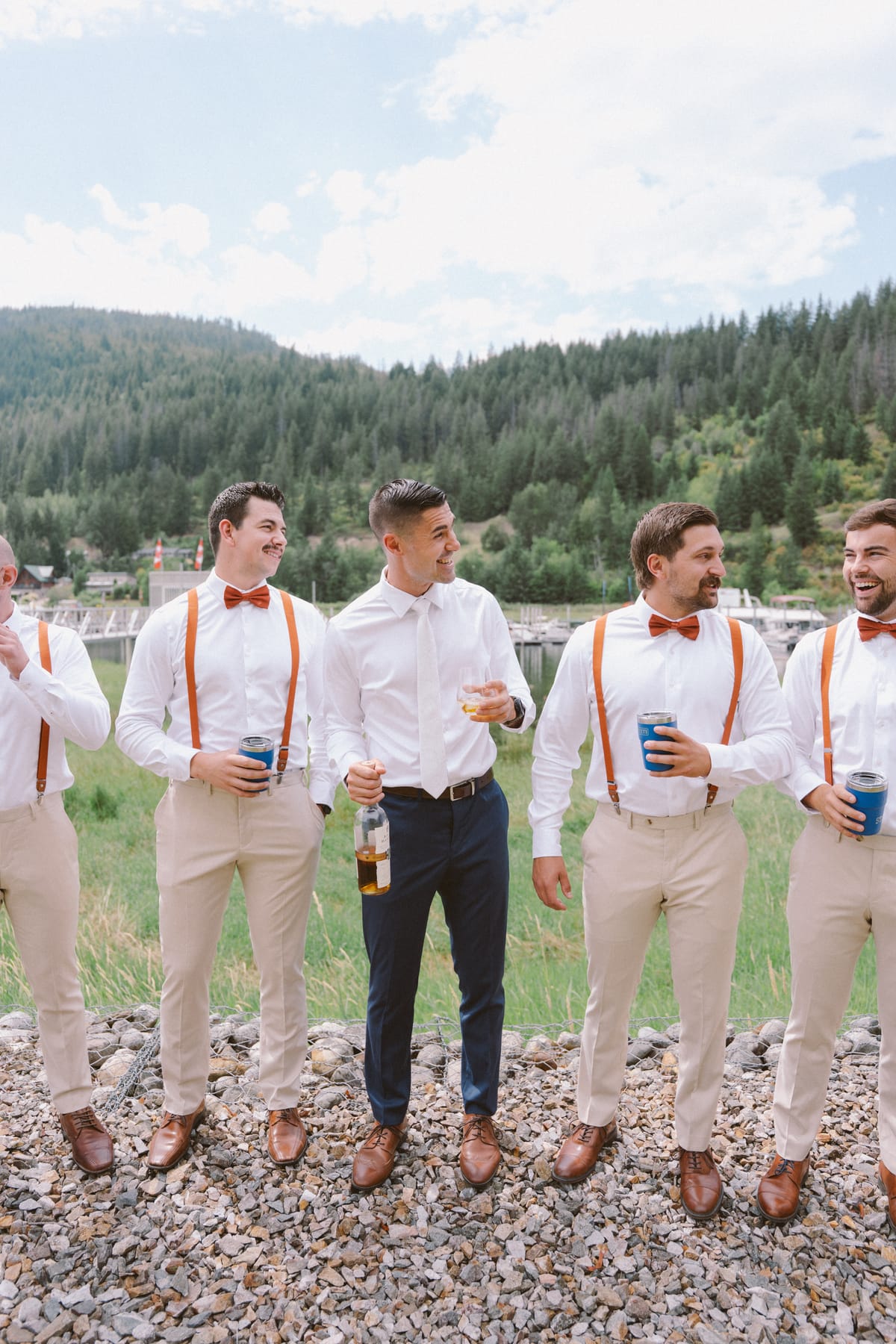Rory with his groomsmen in orange bow ties and suspenders, drinks in hand, mountains behind