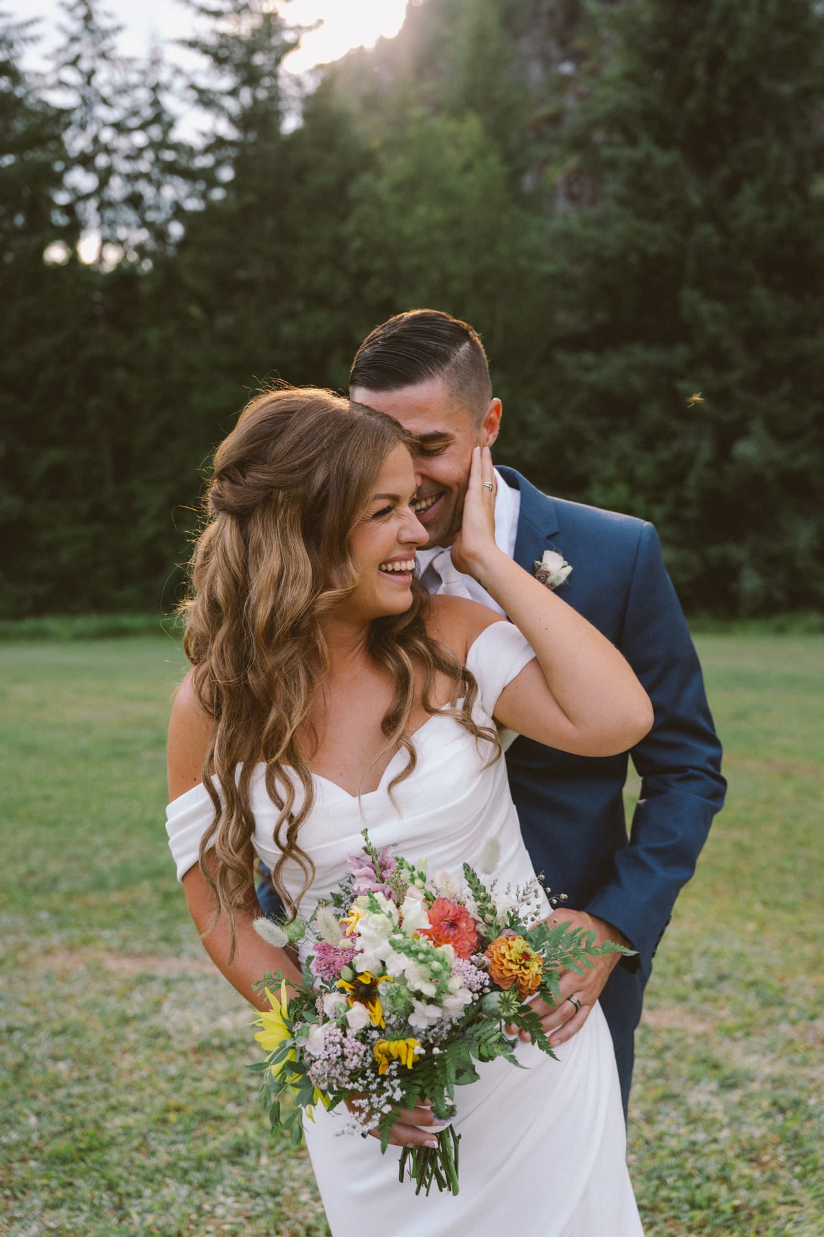 Rory holding Kendra from behind as she laughs, holding her wildflower bouquet