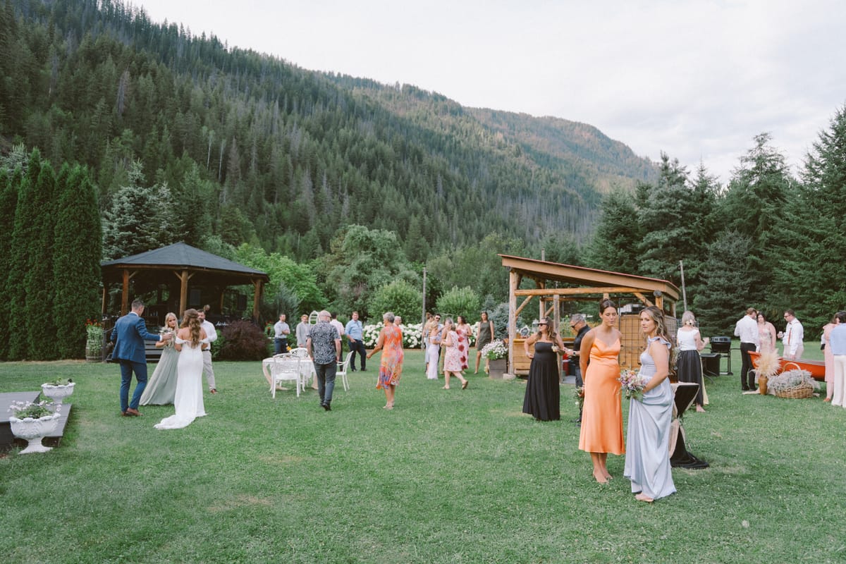 Guests mingling at cocktail hour on the lawn with the gazebo and forested mountains behind