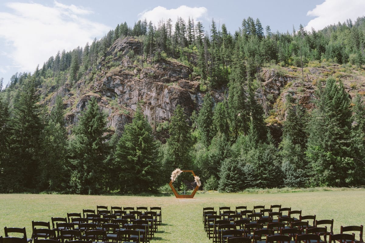 The hexagonal wooden ceremony arch set in the meadow below a towering rock face