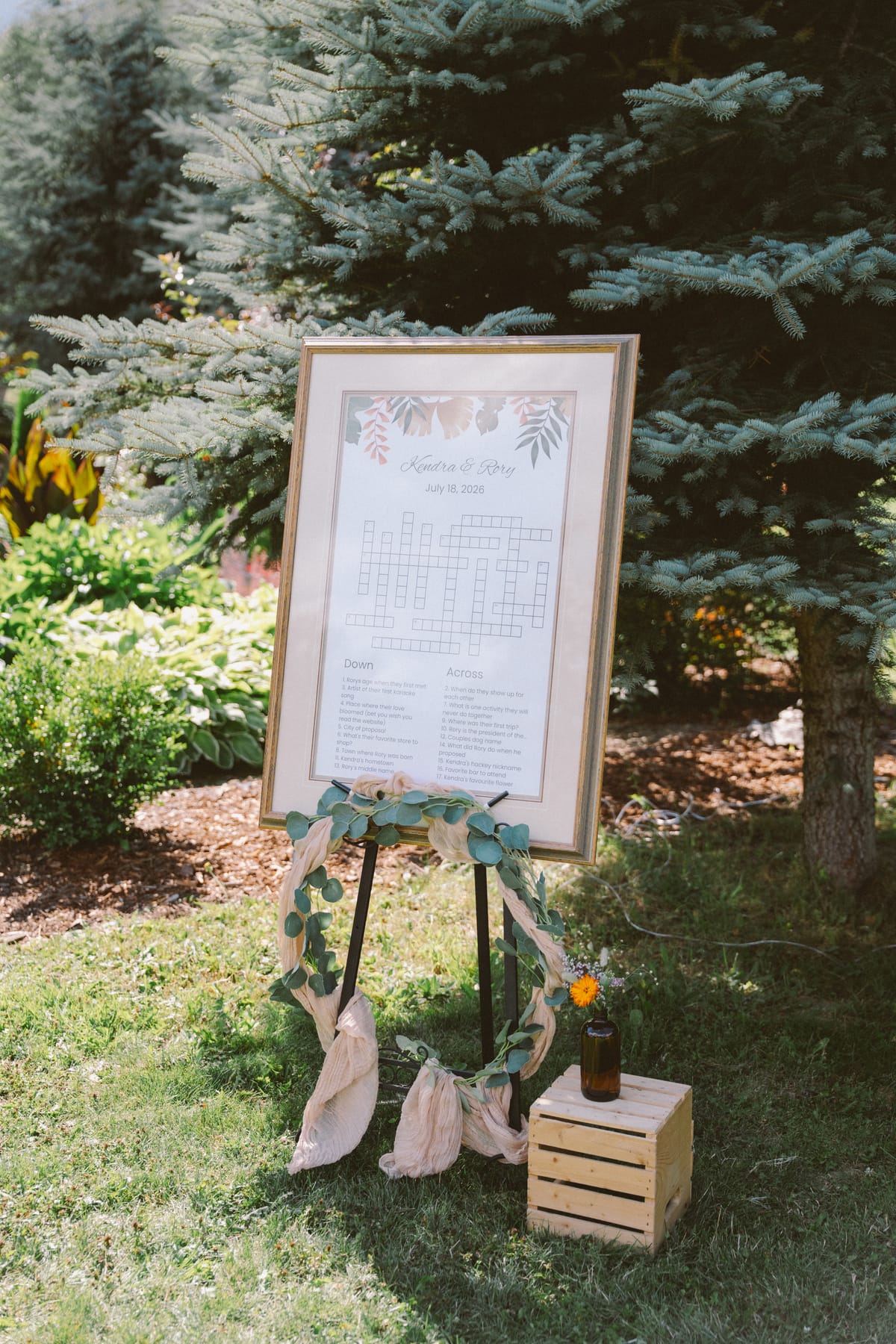 The framed Kendra and Rory crossword welcome sign on an easel with a eucalyptus garland