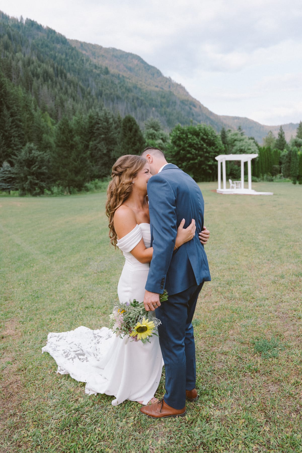 Kendra and Rory sharing a kiss in the meadow with a white gazebo and mountains behind