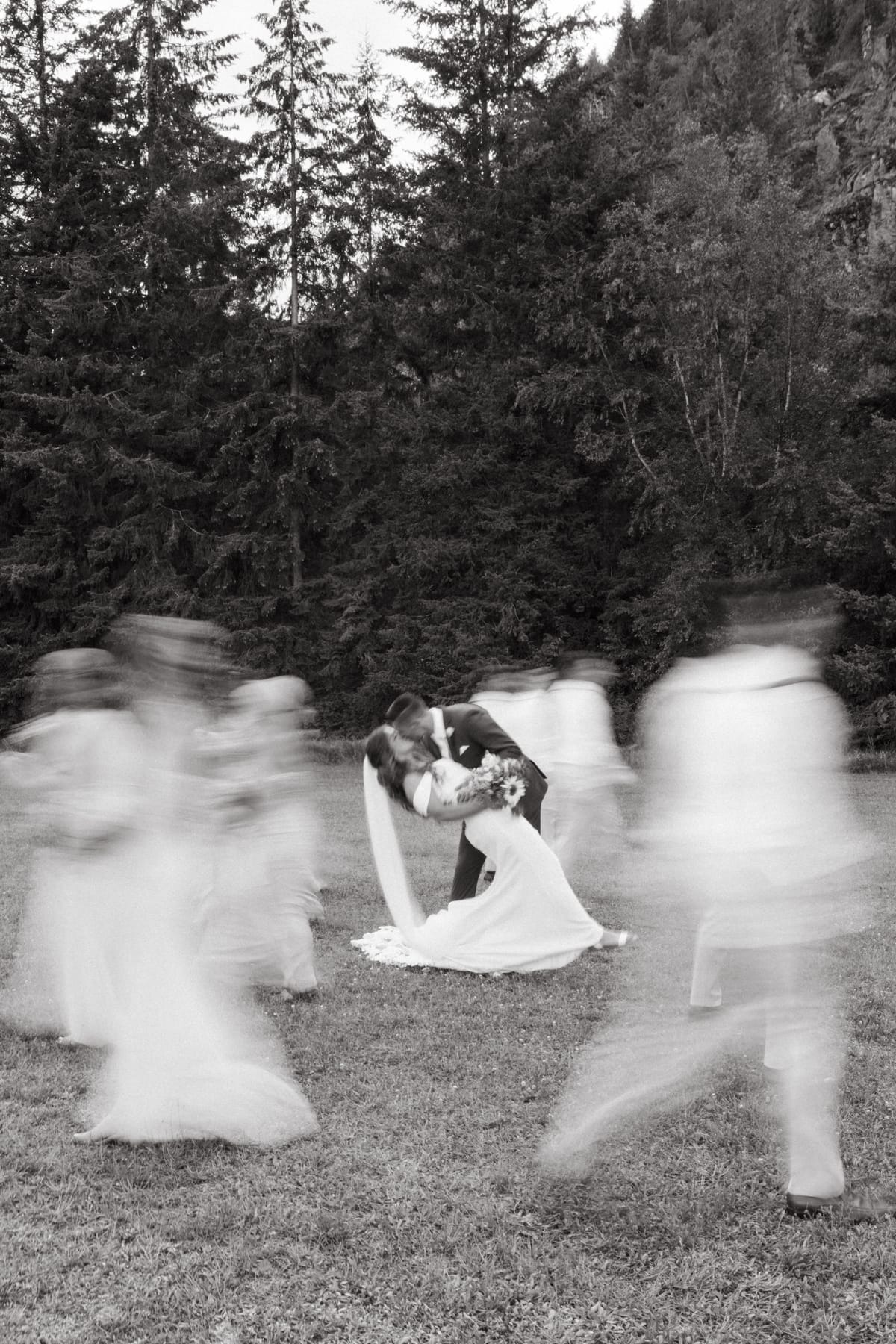 A long-exposure black and white of Kendra and Rory kissing as the wedding party blurs around them