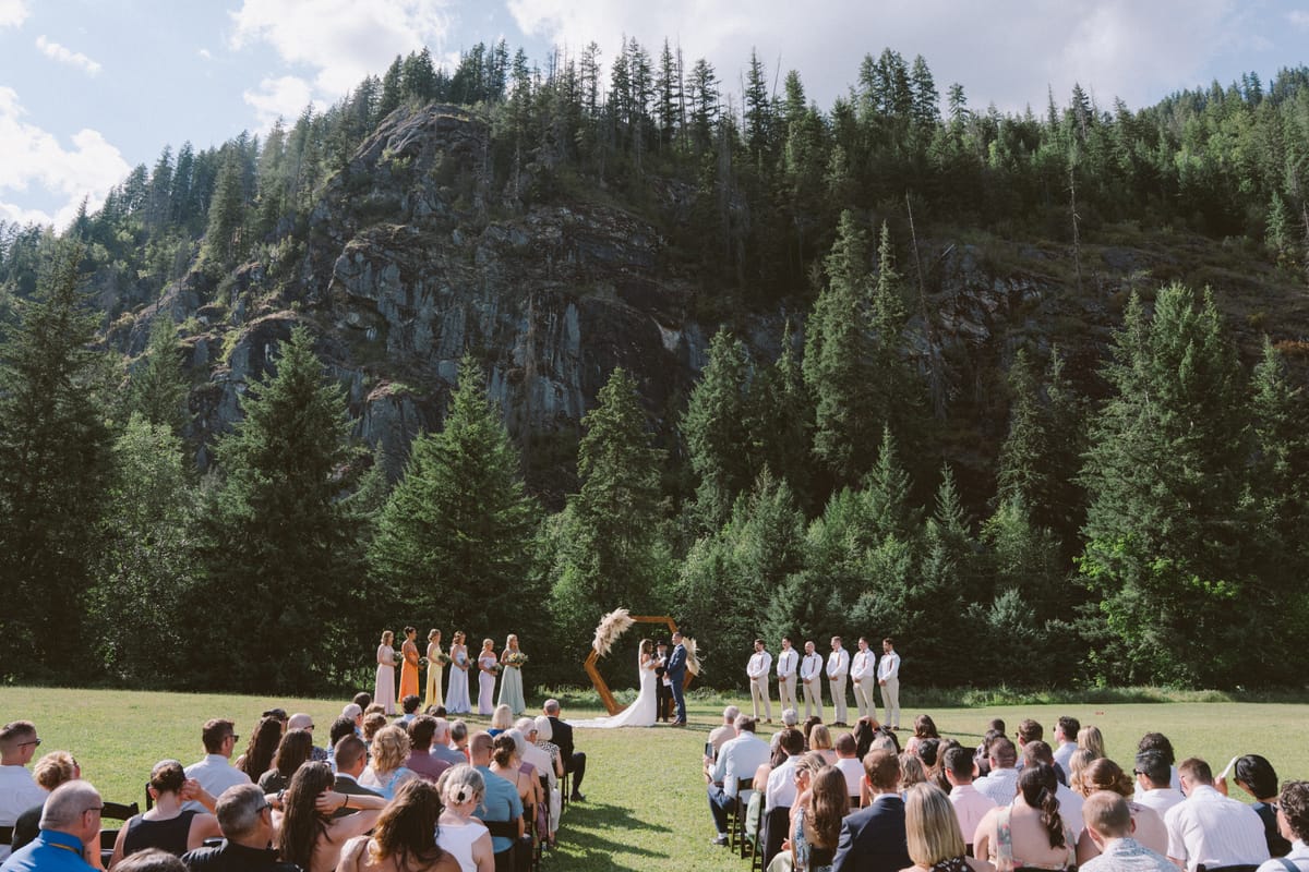 The mountain-meadow ceremony seen from behind the seated guests below the rock face