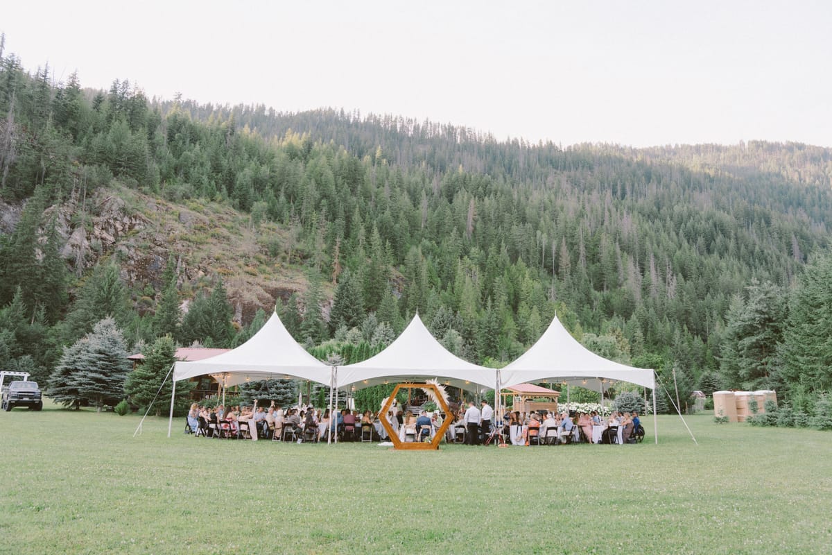 The peaked marquee tents of the reception set in the mountain meadow at dusk