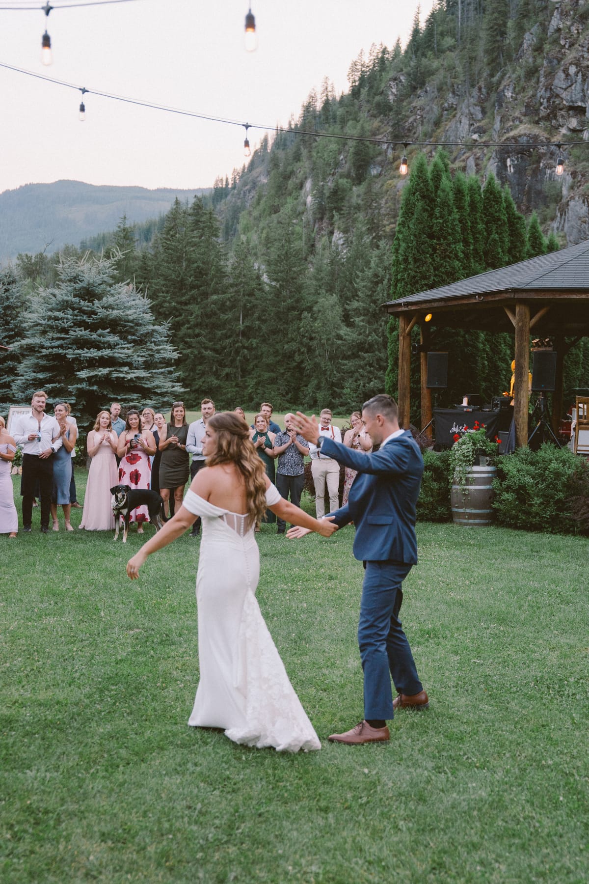 Rory twirling Kendra during the first dance as guests clap, mountain behind