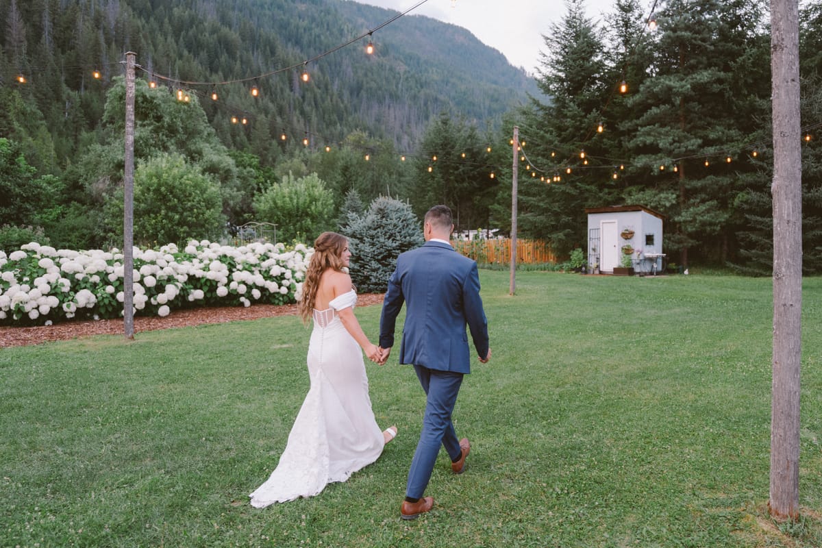 Kendra and Rory walking the lawn hand in hand under string lights at dusk