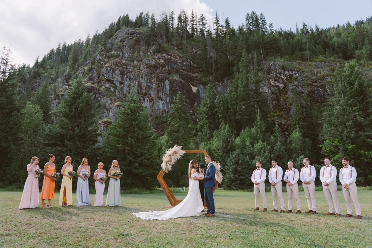 Wide view of Kendra and Rory at the arch with their wedding party and the mountain behind