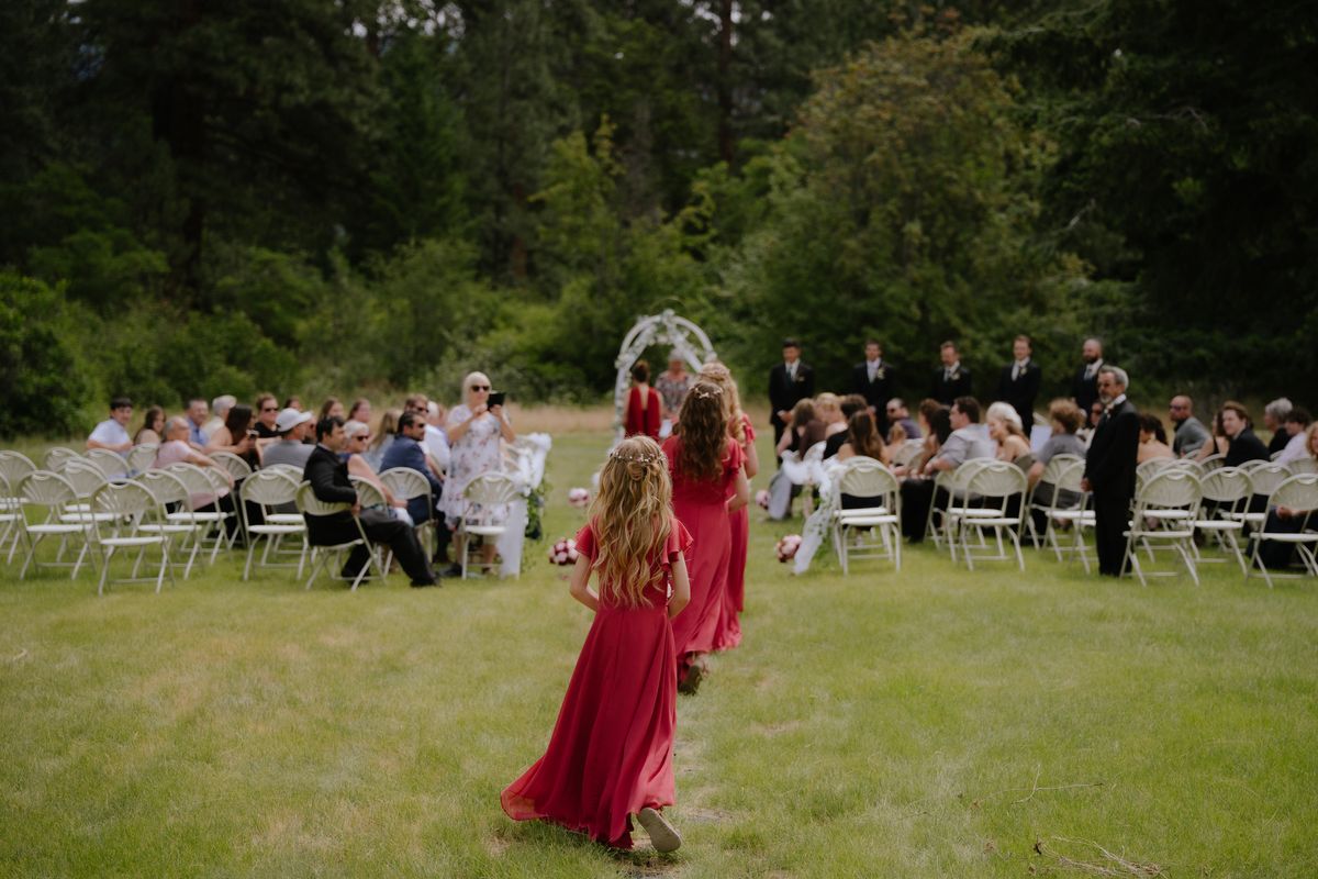 Wide view of the lawn ceremony beneath the floral arch, a flower girl in red