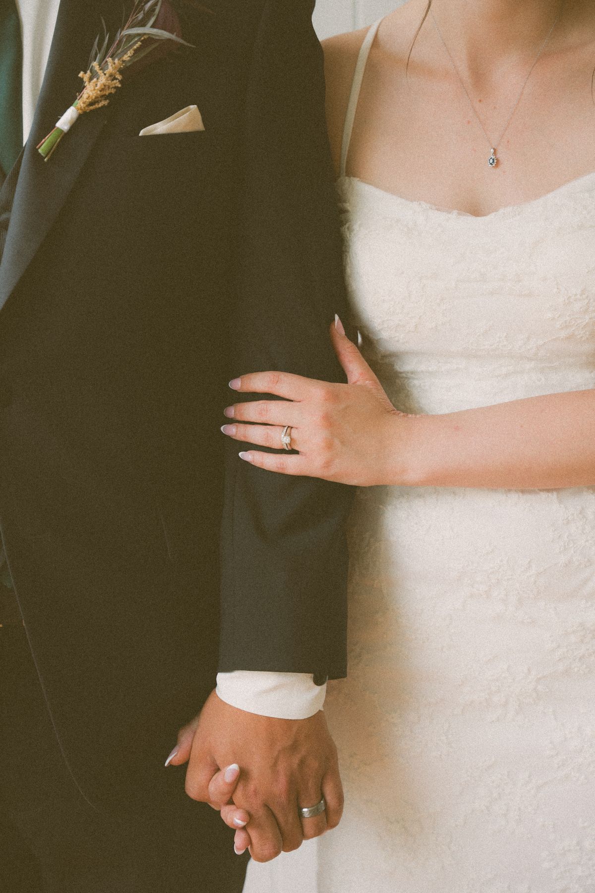 Detail of the couple's hands and rings against the groom's black suit