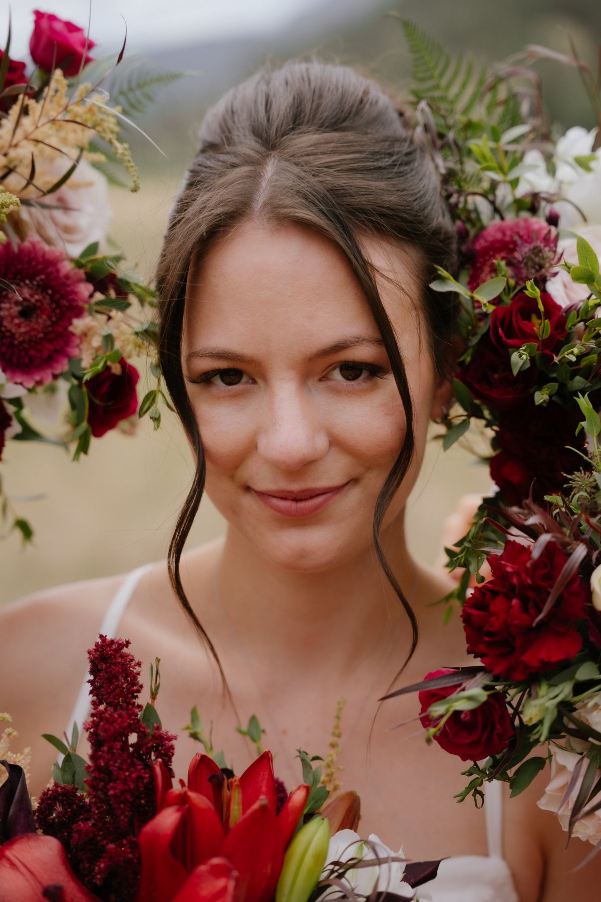 The bride looking to camera framed by burgundy blooms