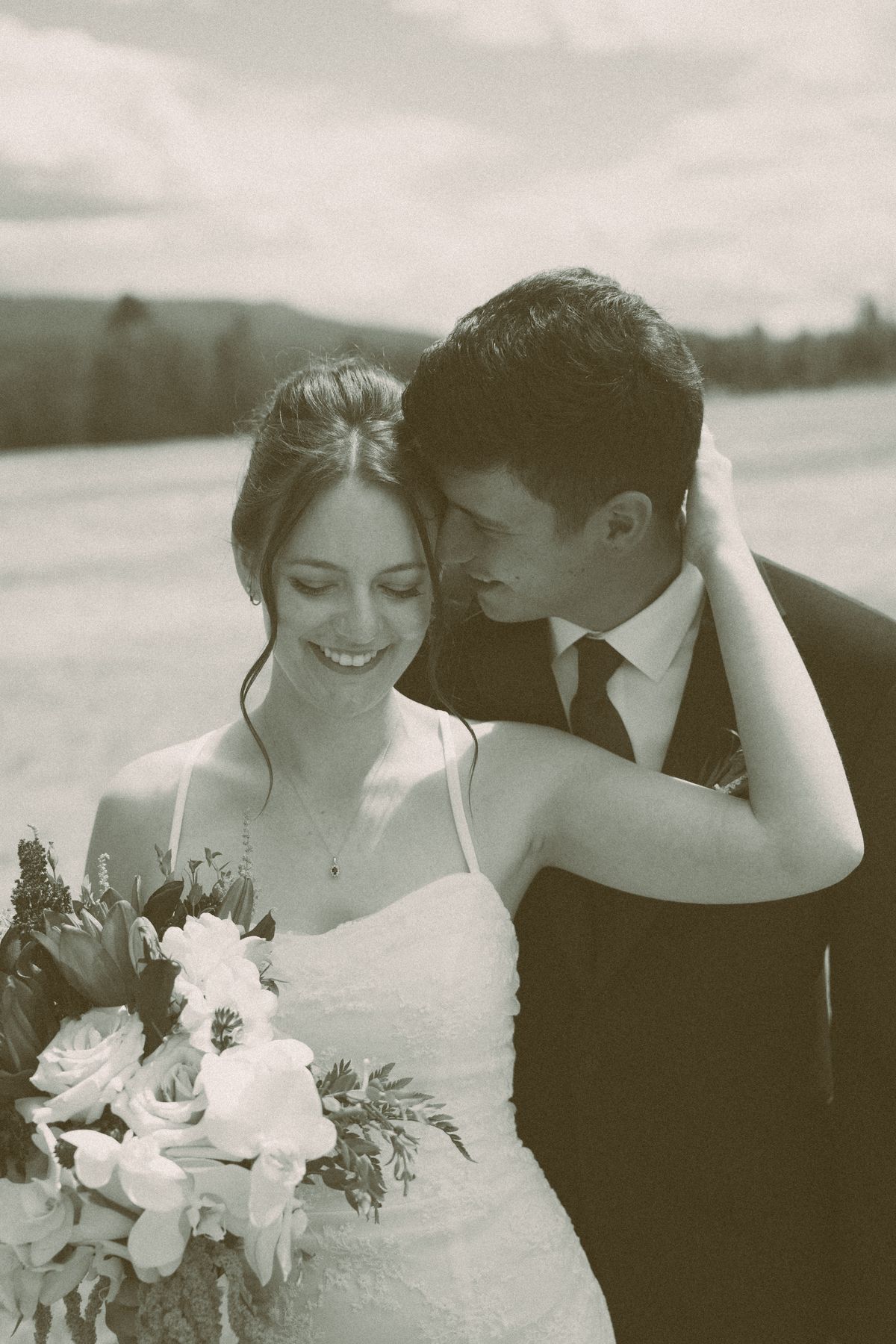 Black and white of the couple close together, the bride's hand at his neck