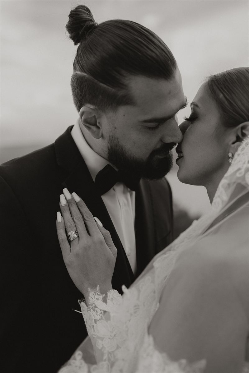Black and white portrait of a couple about to kiss, the bride's hand and wedding ring resting on the groom's lapel