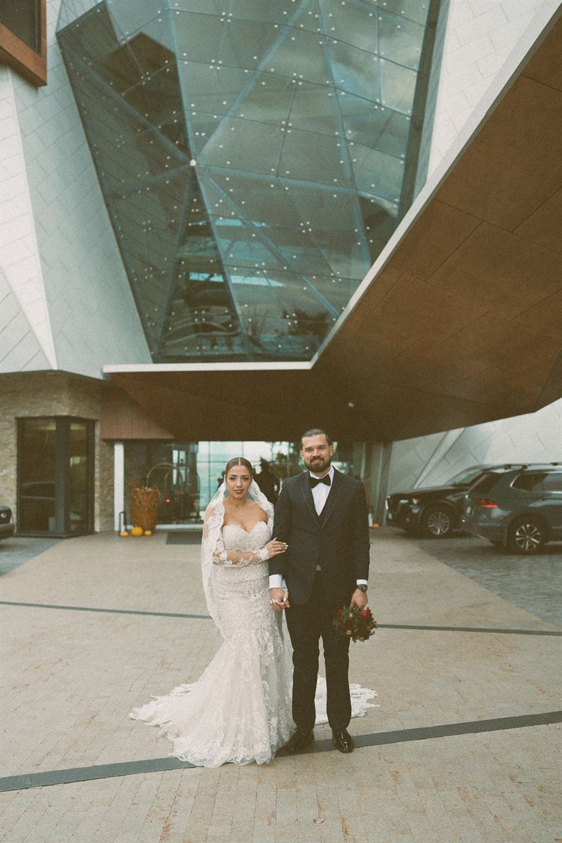Bride and groom standing together beneath the angular glass facade of a modern Okanagan resort