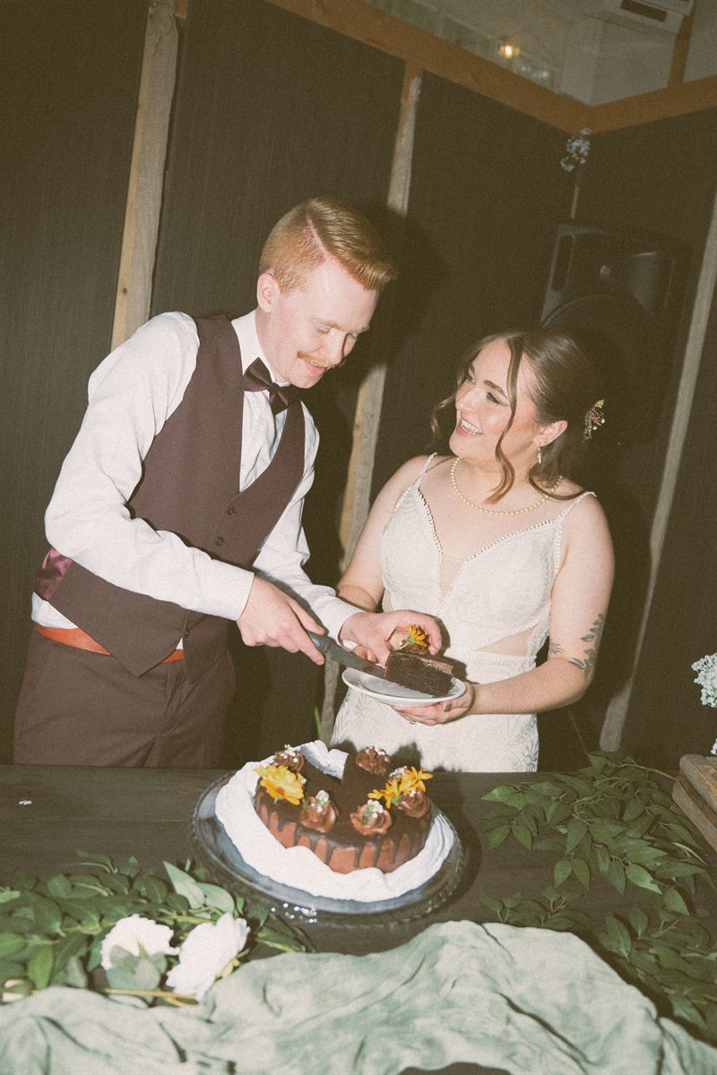 Bride and groom cutting a chocolate cake trimmed with marigolds inside the reception barn