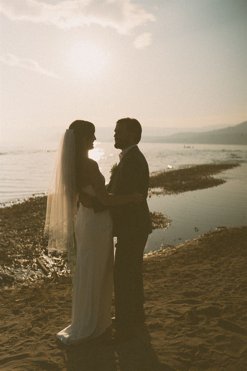Silhouette of a bride and groom on the shore of Okanagan Lake in Kelowna as the sun drops behind the hills