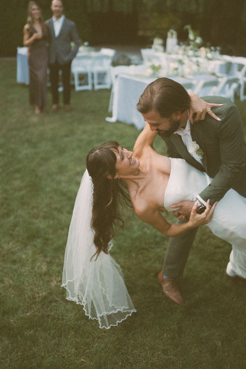 Groom dipping the bride on the reception lawn as she laughs, tables set behind them at a Kelowna wedding